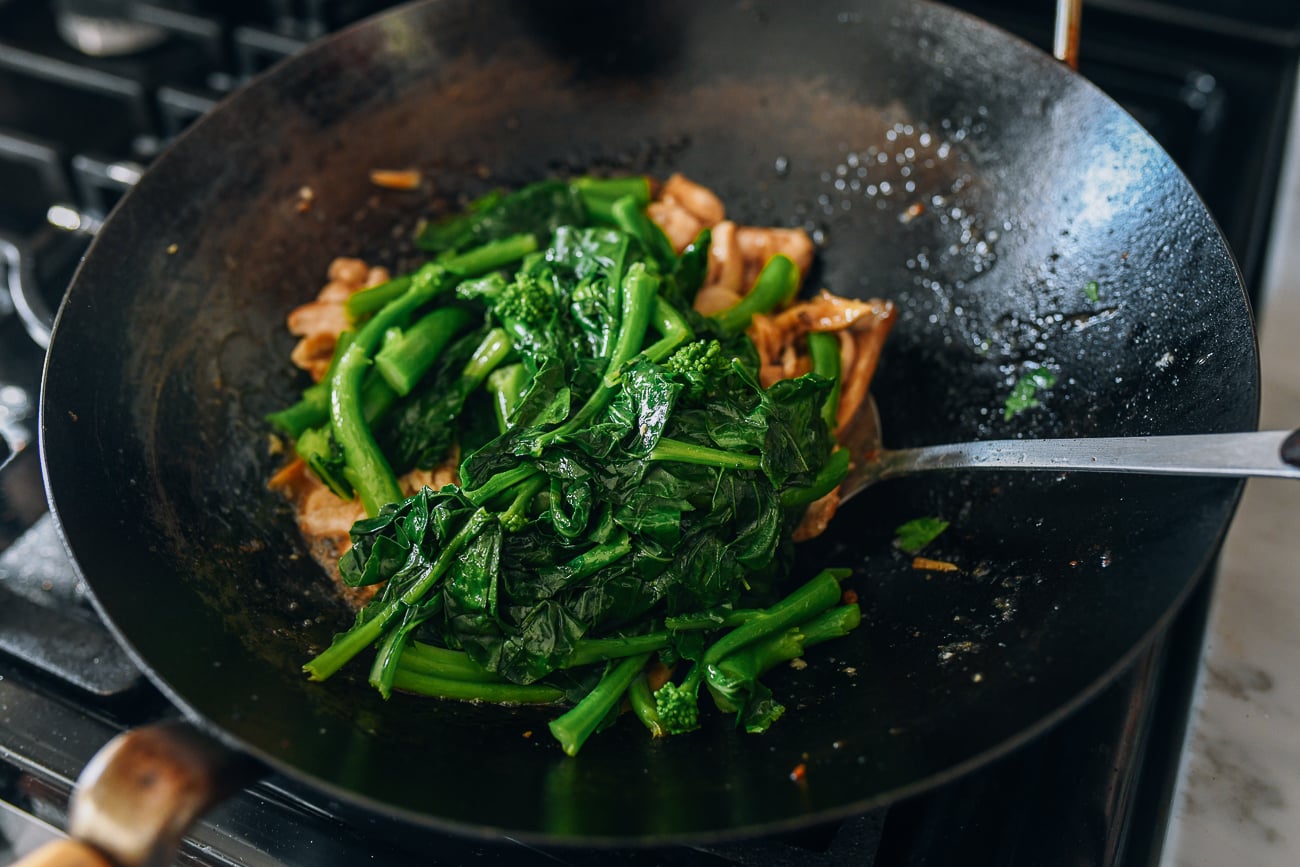 Adding blanched Chinese broccoli to other ingredients in wok