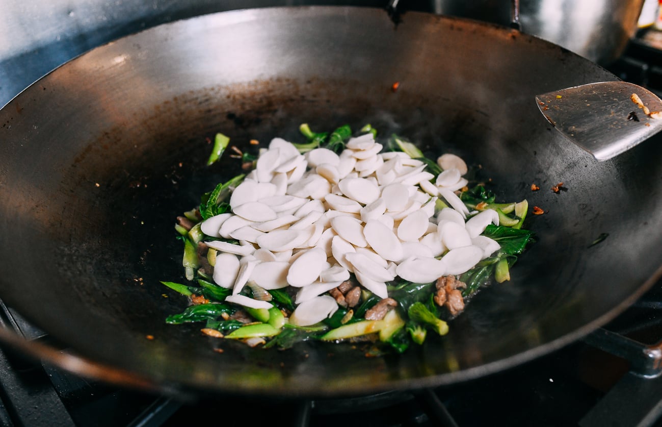 Adding frozen rice cakes on top of bed of greens and pork