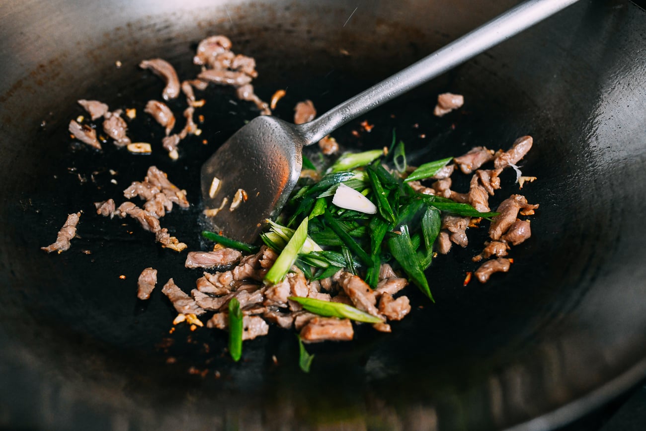 Adding scallions to pork in wok
