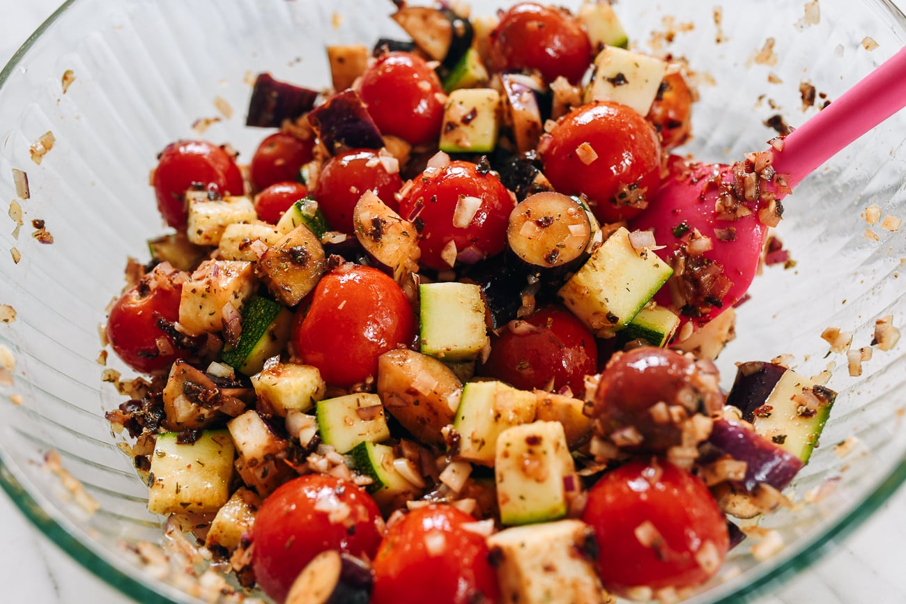 eggplant, zucchini, and cherry tomatoes in glass mixing bowl with seasoning