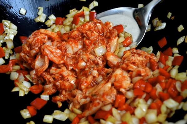 Adding chopped kimchi to onions and peppers in wok