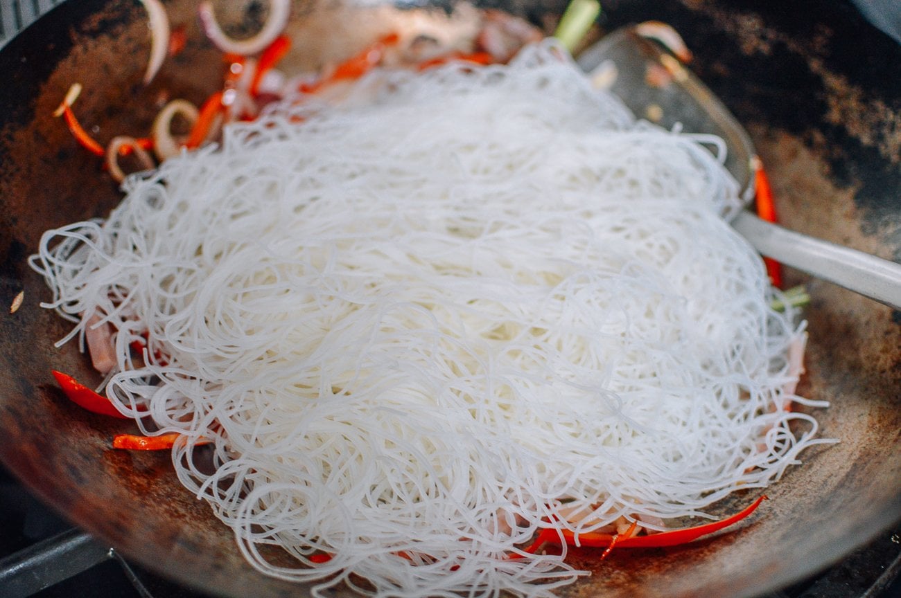 adding rice noodles to meat and vegetables in wok