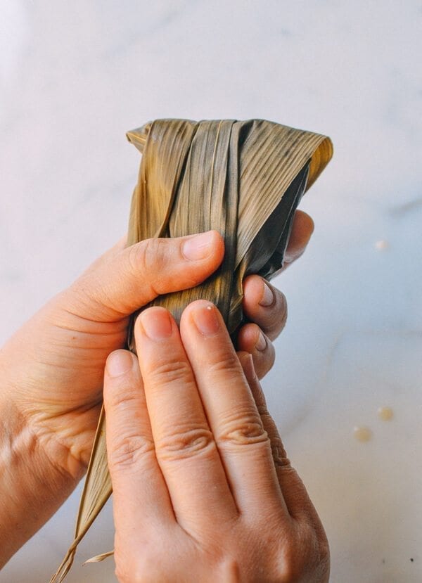 Before you start, there are a few things to remember: You must cut away at least half an inch off the bottom of every leaf you use. Make sure the kitchen twine won’t break easily. To do this, it’s best to wet the twine first by soaking it in a bowl of water. It’s best to tie one end of the twine to an anchor point or kitchen fixture (e.g. you kitchen sink), because you will only have one hand to tie the zongzi. Your other hand will be holding the zongzi. Or have someone help you out! Making zongzi is like making a big batch of dumplings or wontons—all hands on deck! Just make sure that the newbies are holding the strings and the seasoned pros are doing the folding! Hah! If leaves rip anywhere during the wrapping process, you’ll need to start over and discard the ripped leaf. That’s why I call for more leaves than is technically needed. Some of the leaves are bound to get ripped.