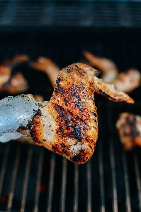 Tongs holding grilled chicken wing