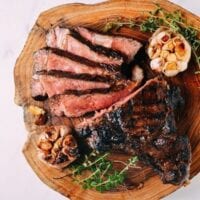 Sliced ribeye steak with roasted garlic on cutting board