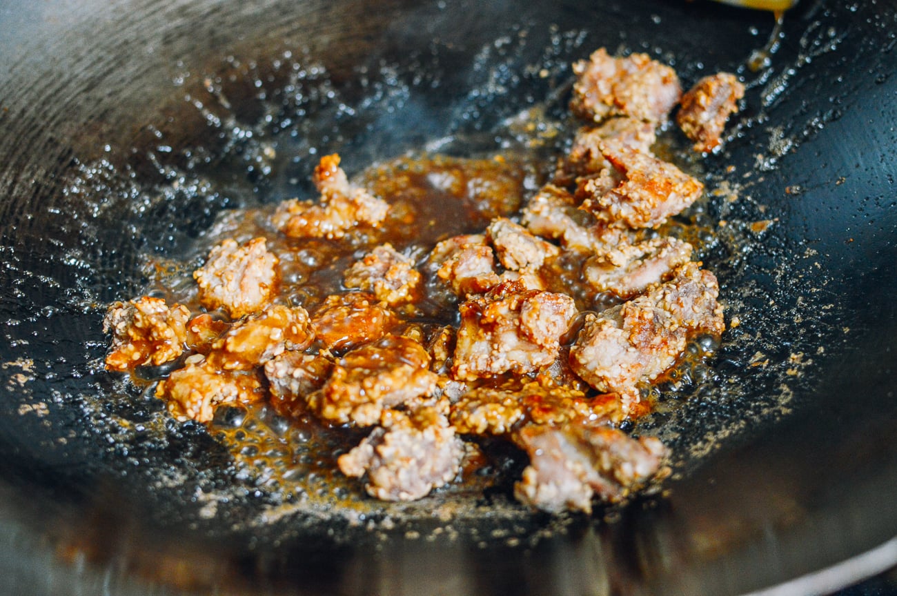 tossing crispy sesame chicken pieces with sauce