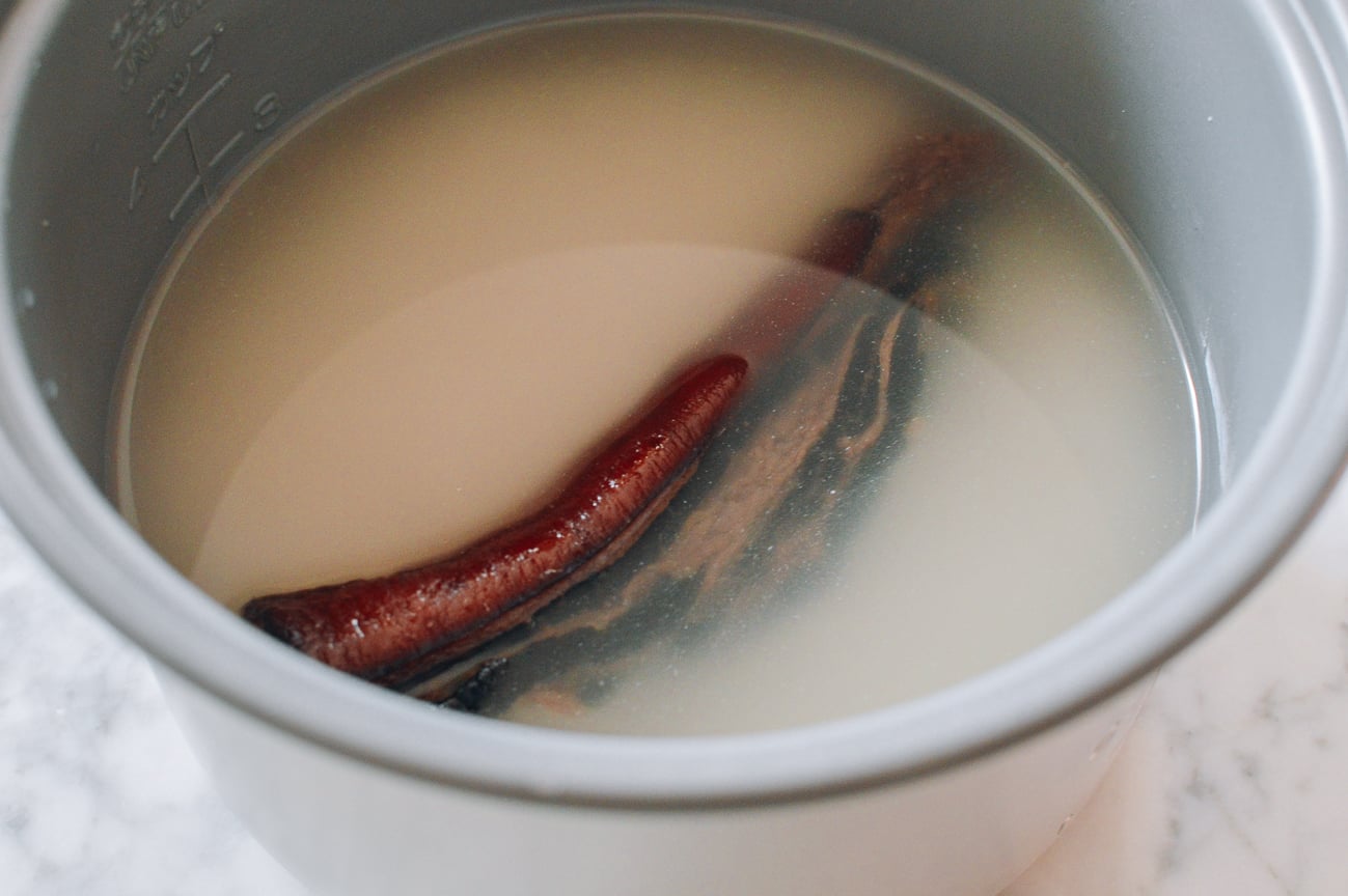 Piece of cured pork belly in rice cooker with rice and water