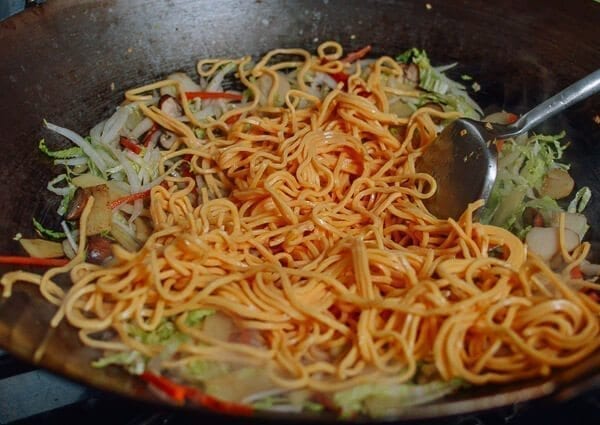 Take the shrimp and noodles out of the refrigerator, and let them come up to room temperature. One trick for the noodles is to soak the whole bag (unopened) in hot water, which speeds up the warming process without making the noodles soggy. If you can’t find lo mein noodles, you can actually substitute dried linguini. Just cook until al dente, drain, and immediately toss with 1 tablespoon of vegetable oil, working the oil into the pasta so the noodles don't stick together. Always prepare your noodles just before you are ready to make the dish, so they don’t dry out and remain at room temperature or warmer. This makes the stir-frying process much easier. Combine the sugar, soy sauces, oyster sauce, sesame oil, and white pepper in a bowl until the sugar is dissolved and set aside. Heat a large wok over high heat until it just starts to smoke, and add 1 tablespoon of oil around the perimeter of the wok. Quickly spread the shrimp around your wok and let them sear for 10-15 seconds on each side. Immediately transfer the shrimp to a plate and set aside. Return the wok to the highest heat possible and add 2 tablespoons oil, along with the garlic. After a few seconds, add the mushrooms, carrots, bamboo shoots, and water chestnuts and stir-fry for 30 seconds. Next, spread the Shaoxing wine around the perimeter of the wok, and then add the napa cabbage. Stir-fry for another 30 seconds. Spread the noodles evenly over the vegetables and give everything a good stir for 1 minute. Now, you can see why you want everything at room temperature, or everything will be overcooked and mushy by the time it heats up! At this point, the noodles should be softened, so add in the sauce mixture you set aside earlier and mix until everything is well combined. Stir-fry for another 30 seconds using a scooping motion, until the sauce is well distributed. Add in the shrimp, snow peas, bean sprouts, and scallions. Mix well for another 2 minutes and serve!