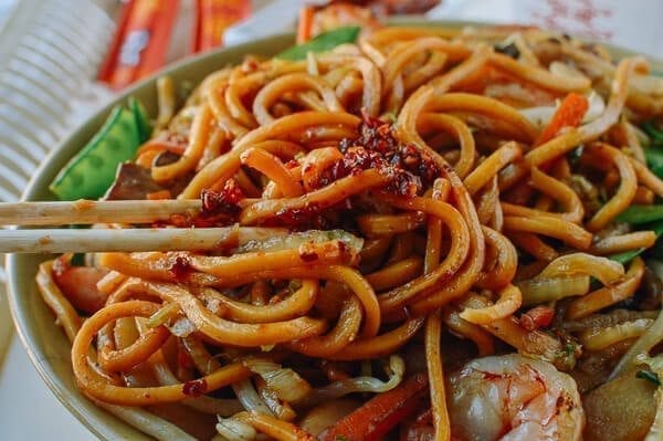 Take the shrimp and noodles out of the refrigerator, and let them come up to room temperature. One trick for the noodles is to soak the whole bag (unopened) in hot water, which speeds up the warming process without making the noodles soggy. If you can’t find lo mein noodles, you can actually substitute dried linguini. Just cook until al dente, drain, and immediately toss with 1 tablespoon of vegetable oil, working the oil into the pasta so the noodles don't stick together. Always prepare your noodles just before you are ready to make the dish, so they don’t dry out and remain at room temperature or warmer. This makes the stir-frying process much easier. Combine the sugar, soy sauces, oyster sauce, sesame oil, and white pepper in a bowl until the sugar is dissolved and set aside. Heat a large wok over high heat until it just starts to smoke, and add 1 tablespoon of oil around the perimeter of the wok. Quickly spread the shrimp around your wok and let them sear for 10-15 seconds on each side. Immediately transfer the shrimp to a plate and set aside. Return the wok to the highest heat possible and add 2 tablespoons oil, along with the garlic. After a few seconds, add the mushrooms, carrots, bamboo shoots, and water chestnuts and stir-fry for 30 seconds. Next, spread the Shaoxing wine around the perimeter of the wok, and then add the napa cabbage. Stir-fry for another 30 seconds. Spread the noodles evenly over the vegetables and give everything a good stir for 1 minute. Now, you can see why you want everything at room temperature, or everything will be overcooked and mushy by the time it heats up! At this point, the noodles should be softened, so add in the sauce mixture you set aside earlier and mix until everything is well combined. Stir-fry for another 30 seconds using a scooping motion, until the sauce is well distributed. Add in the shrimp, snow peas, bean sprouts, and scallions. Mix well for another 2 minutes and serve!