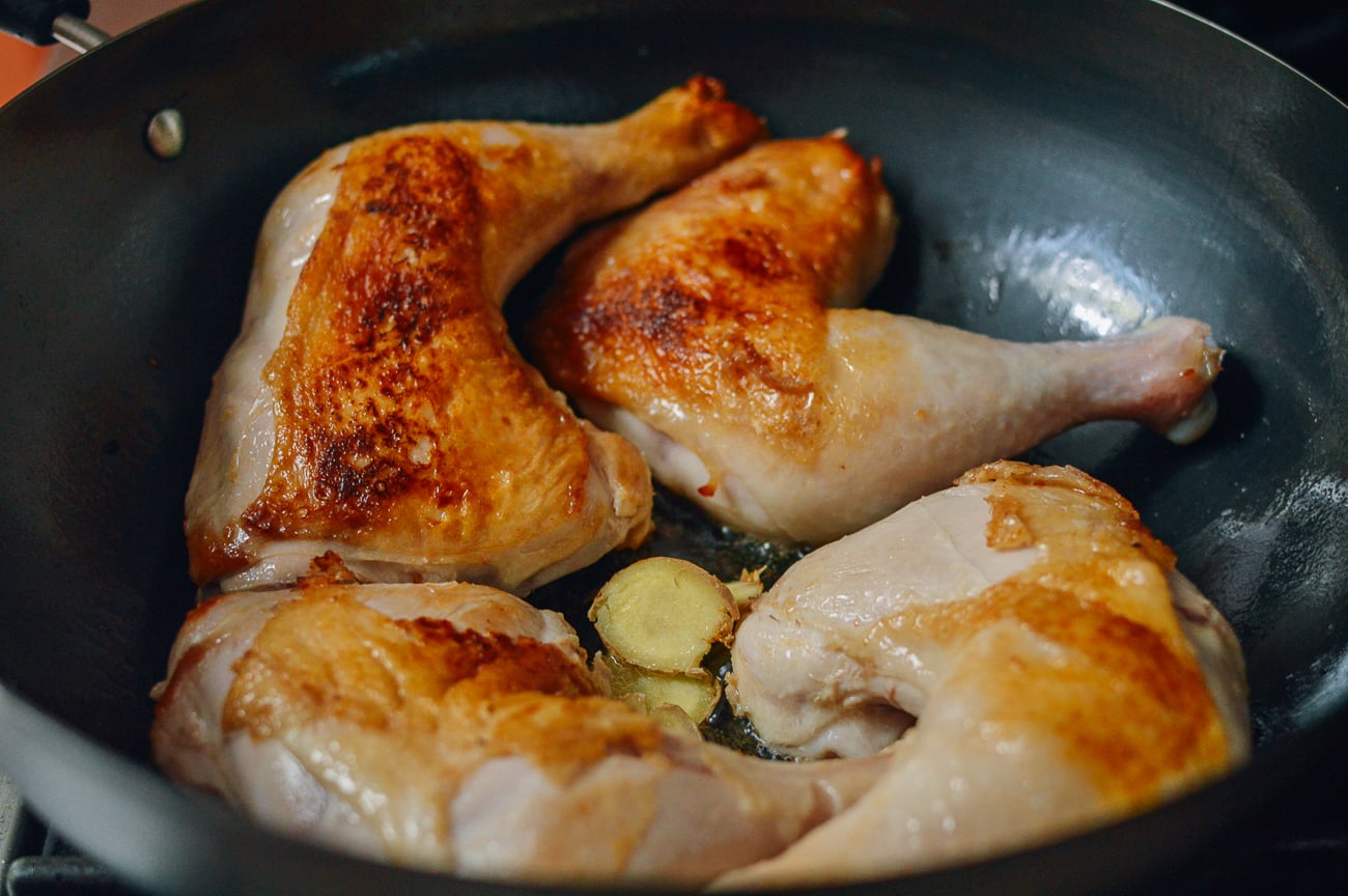 seared chicken leg quarters in wok with ginger slices