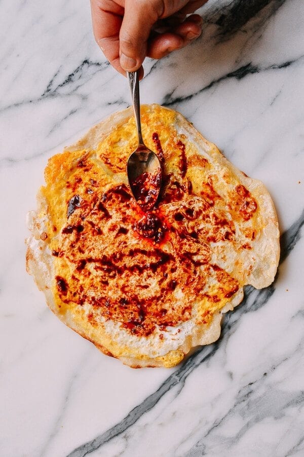 spreading sauce on Jidan Bing: The Chinese Breakfast of Champions, by thewoksoflife.com