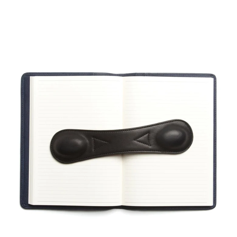 leather book weight placed on a white and black notebook