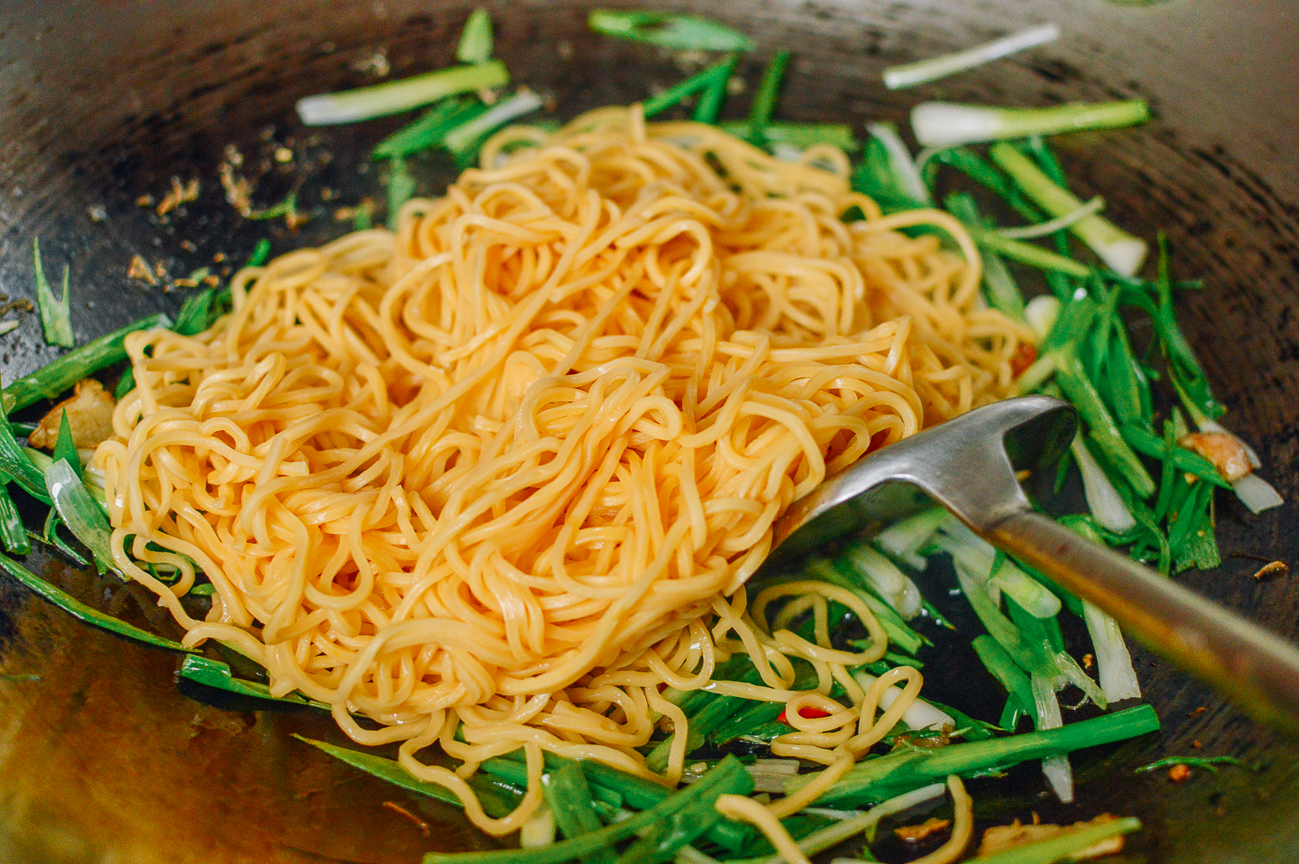 adding hokkien noodles to wok with scallions