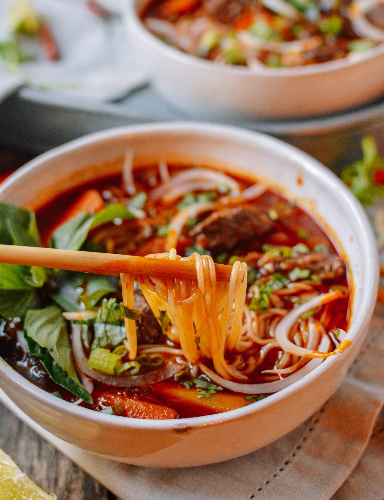 chopsticks picking up rice noodles from bowl of spicy Vietnamese beef stew