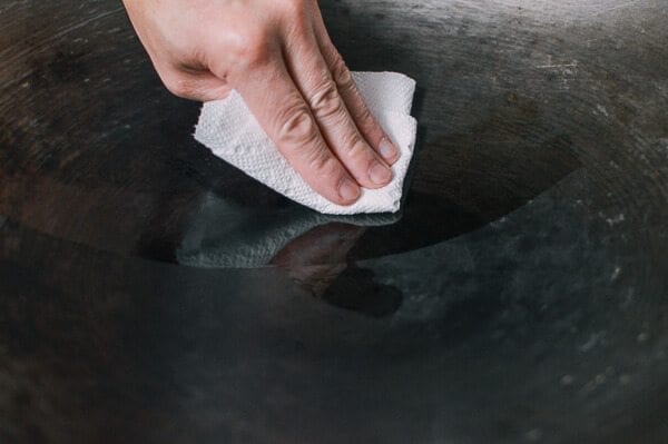 Wiping oil onto wok with paper towel