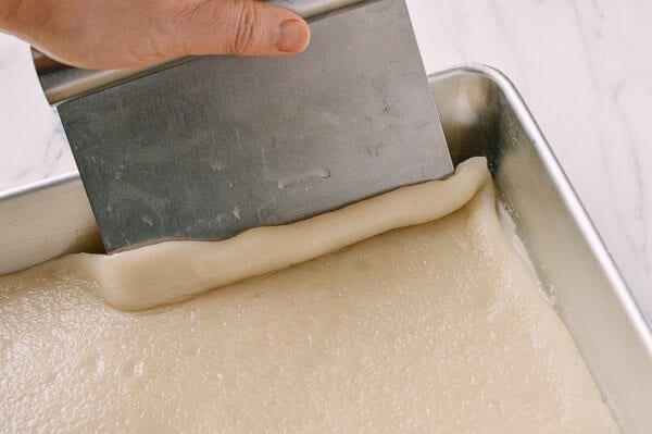 Using an oiled bench scraper to lift mochi off of pan