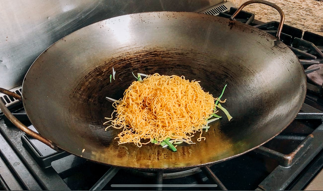 adding noodles to scallions in wok