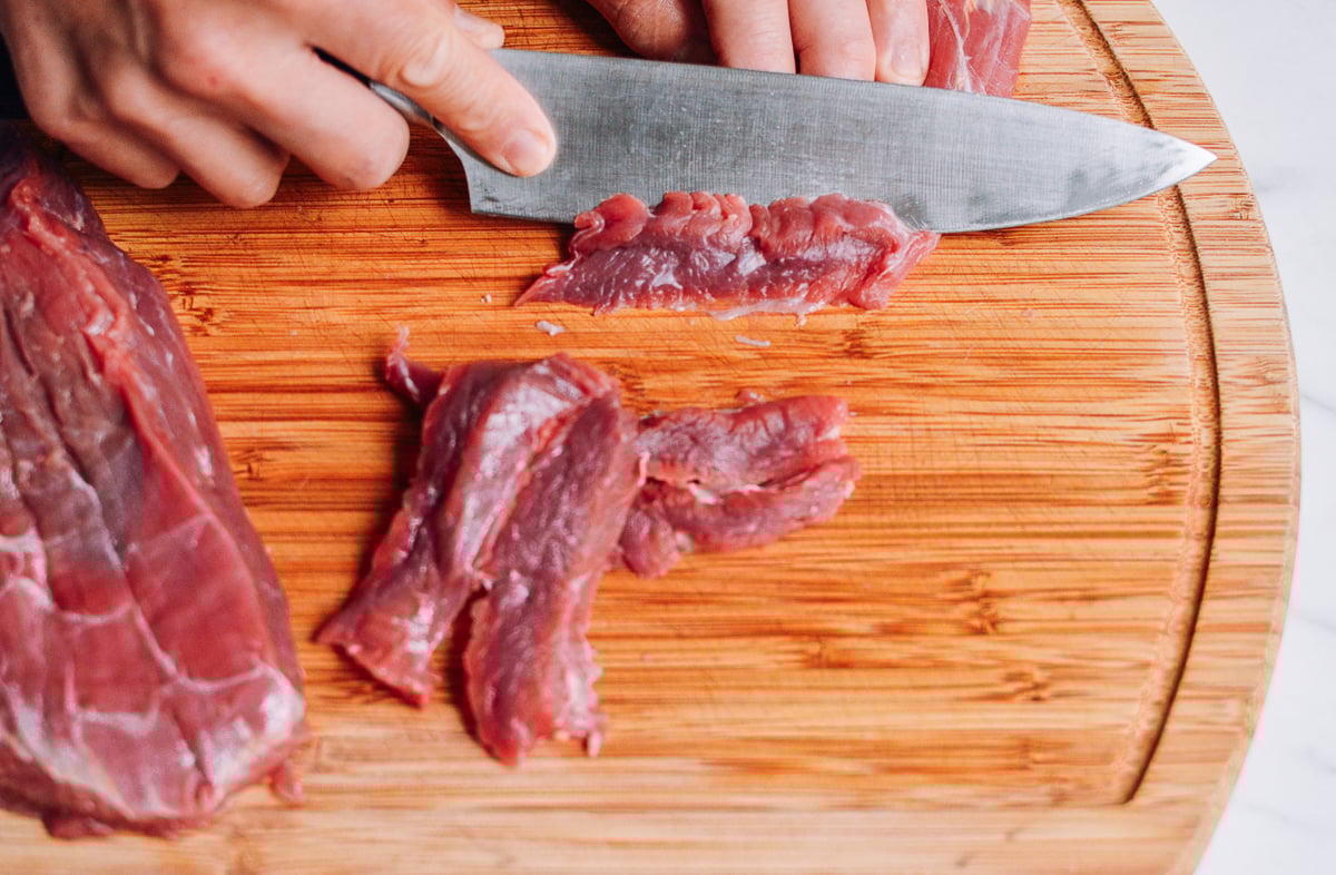 slicing beef flank steak on a cutting board by thewoksoflife.com