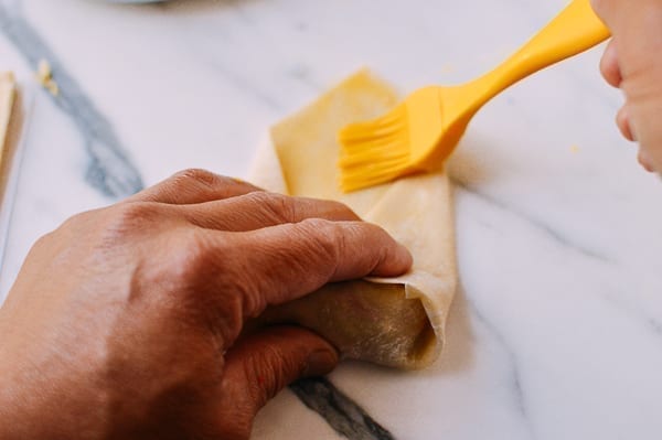 Brushing egg roll wrapper with egg wash to seal, thewoksoflife.com