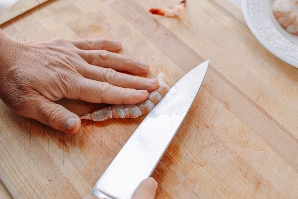 Slicing into the back of a peeled shrimp with chef's knife