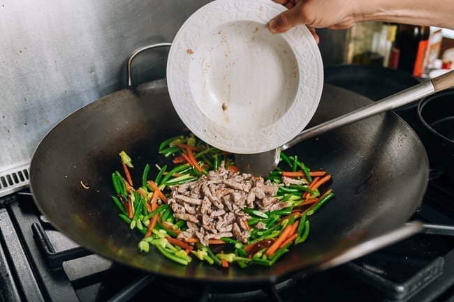 Adding the pre-cooked pork back to stir-fry in wok