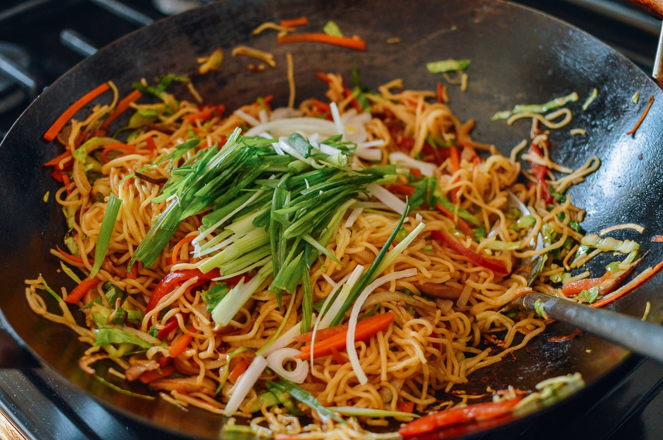 julienned scallions added to noodles in wok