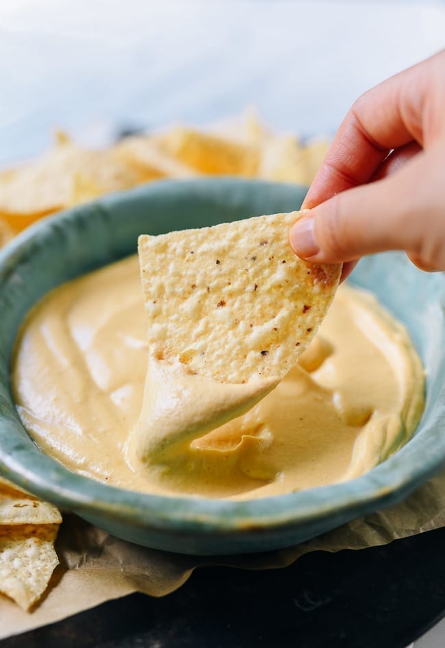 Dipping tortilla chip into plain vegan queso, thewoksoflife.com