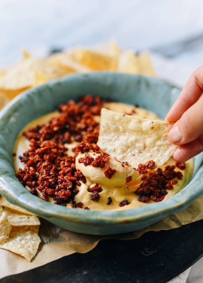 Dipping chip into vegan queso, thewoksoflife.com