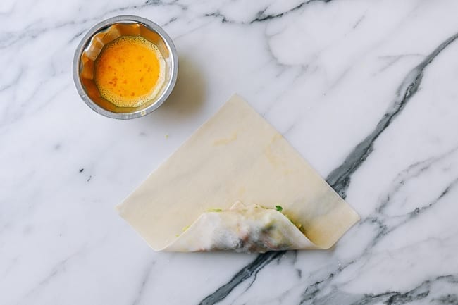 Rolling corner of egg roll wrapper over filling, thewoksoflife.com