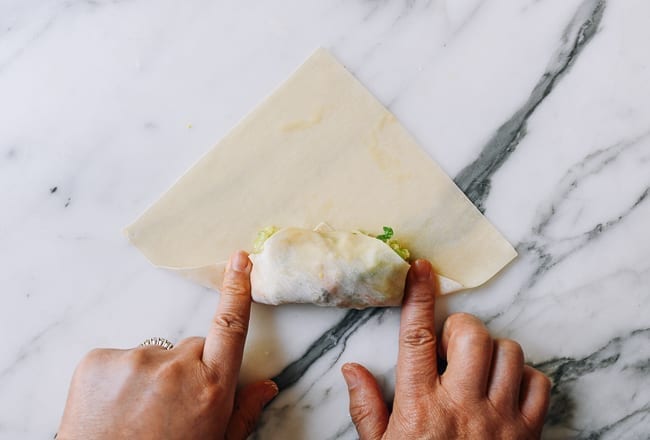 Pressing down egg roll wrapper on both sides of filling, thewoksoflife.com