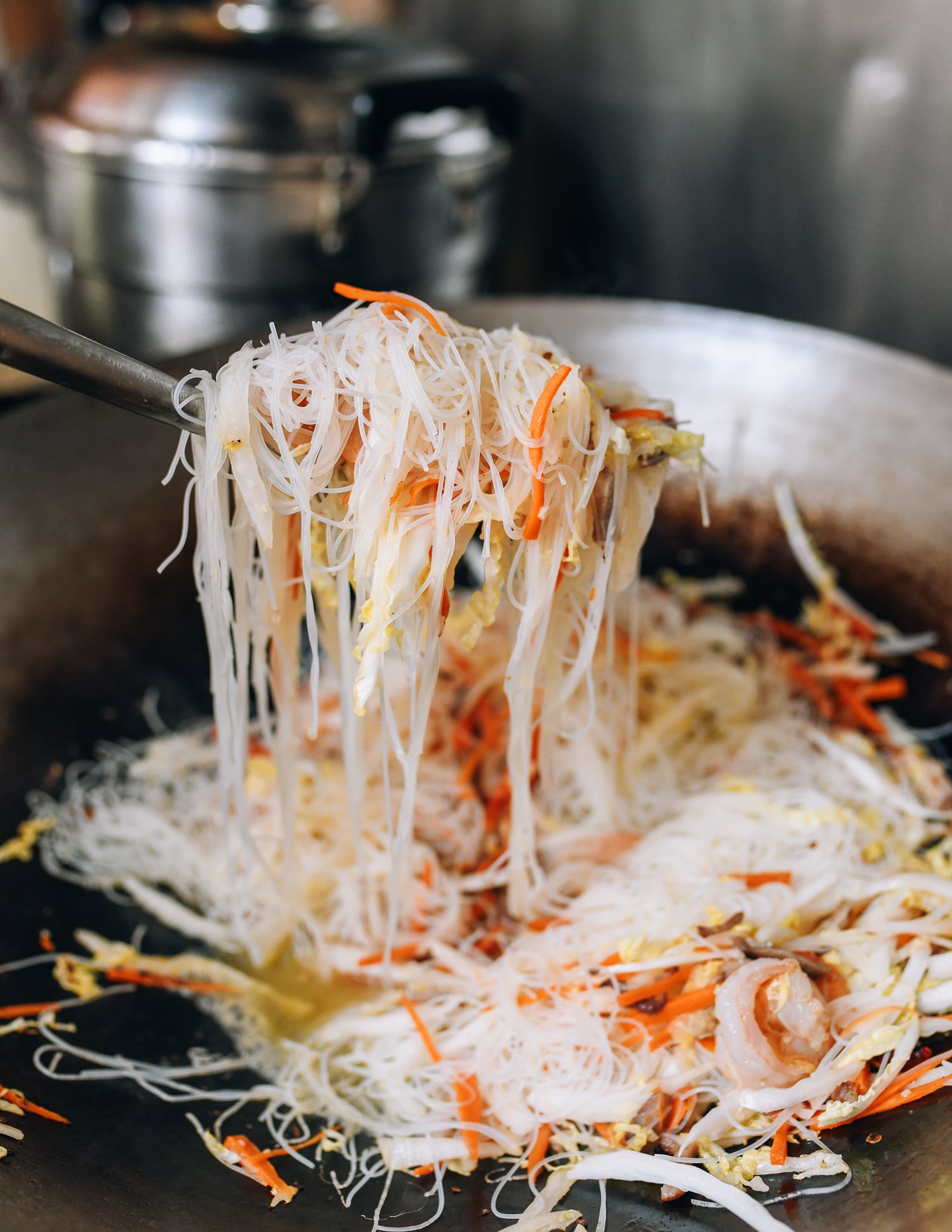 Lifting rice noodles with wok spatula to loosen them, thewoksoflife.com