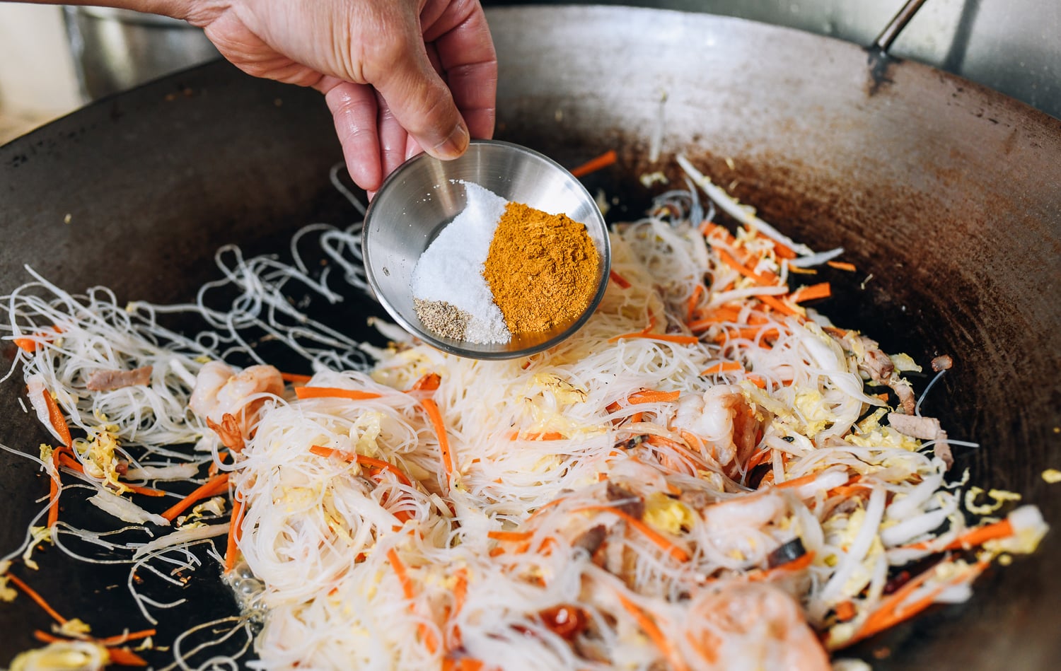 Adding curry powder, salt, sugar, and white pepper to noodles in wok, thewoksoflife.com
