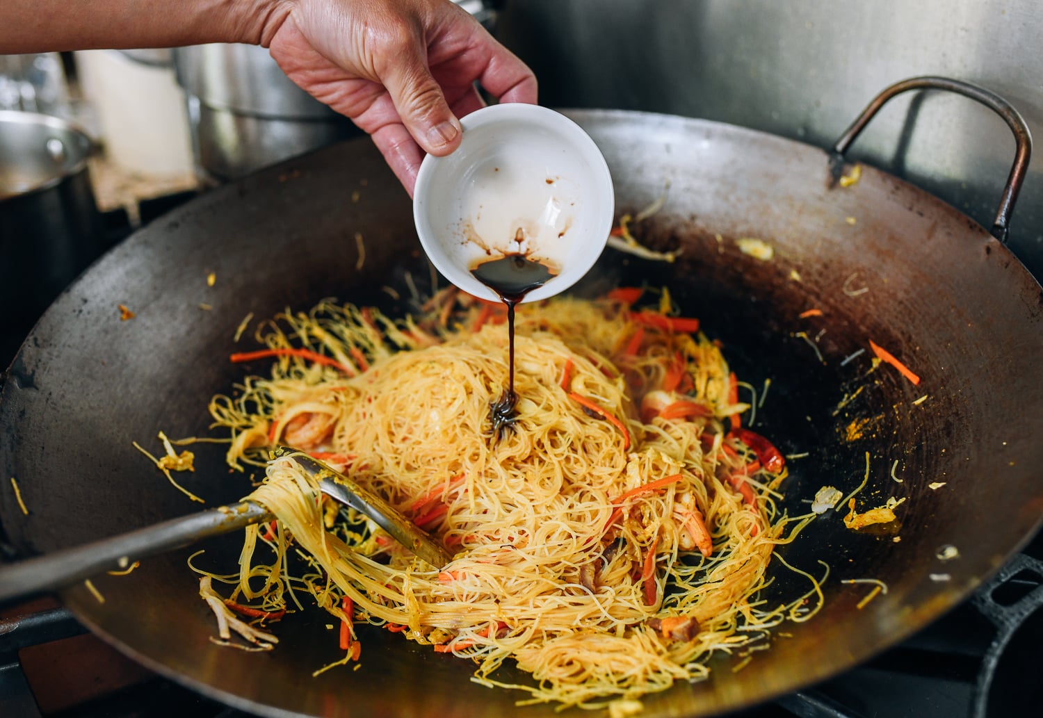 Adding sesame oil and soy sauce to singapore noodles in wok, thewoksoflife.com