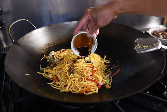 Adding pre-mixed sauce to lo mein in wok, thewoksoflife.com