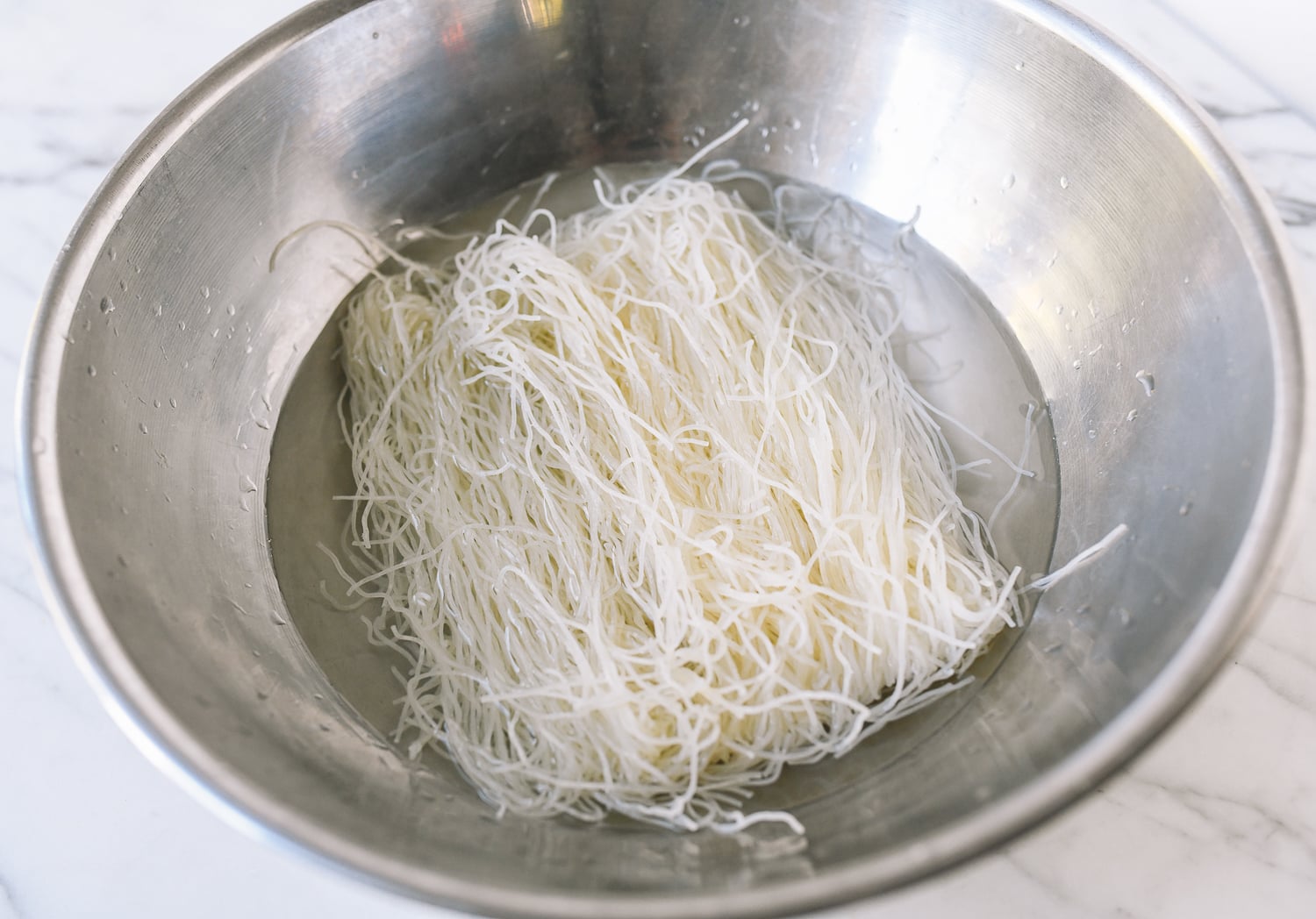 Soaking rice noodles in water in metal bowl, thewoksoflife.com