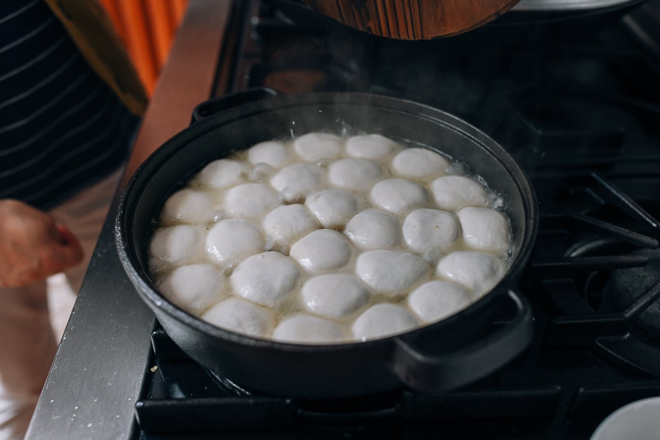 Water sizzling and bubbling in pan of Shengjian bao, thewoksoflife.com