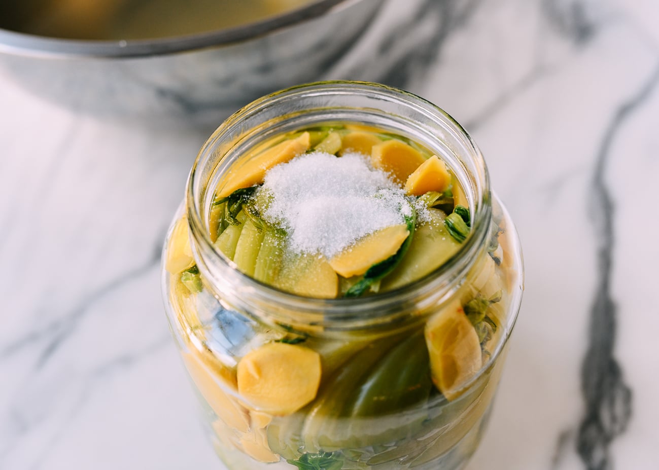 Salt and sugar on top of greens in pickling jar
