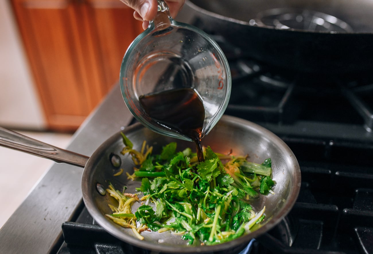 Pouring soy sauce over scallions, ginger, and cilantro