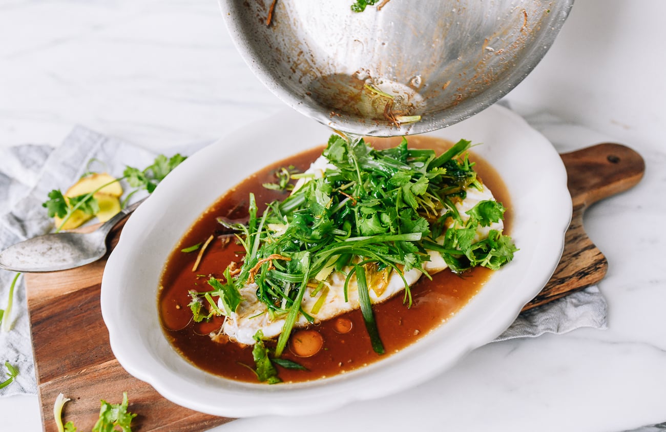 Pouring hot oil over ginger, scallions, and cilantro on Cantonese steamed fish