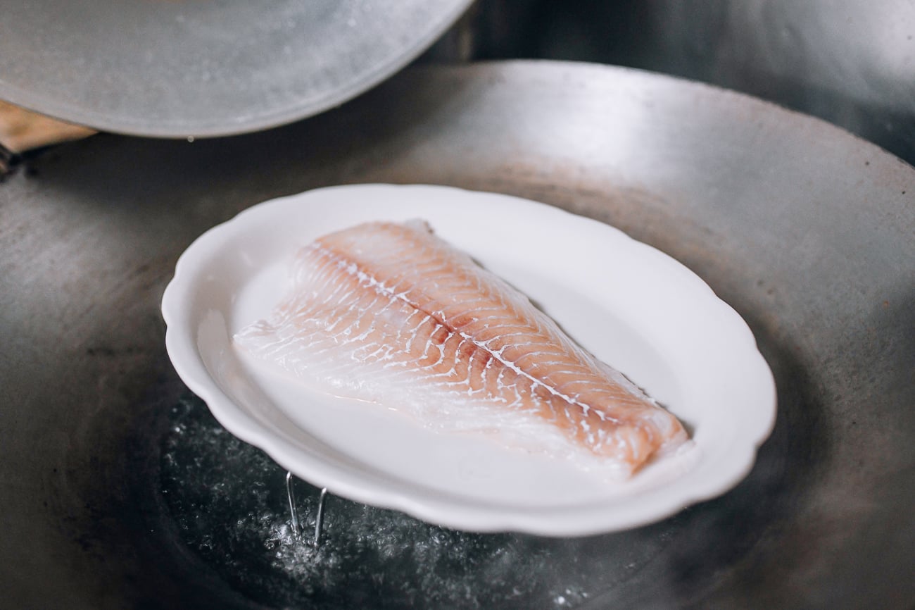 Placing plate of fish in wok to steam