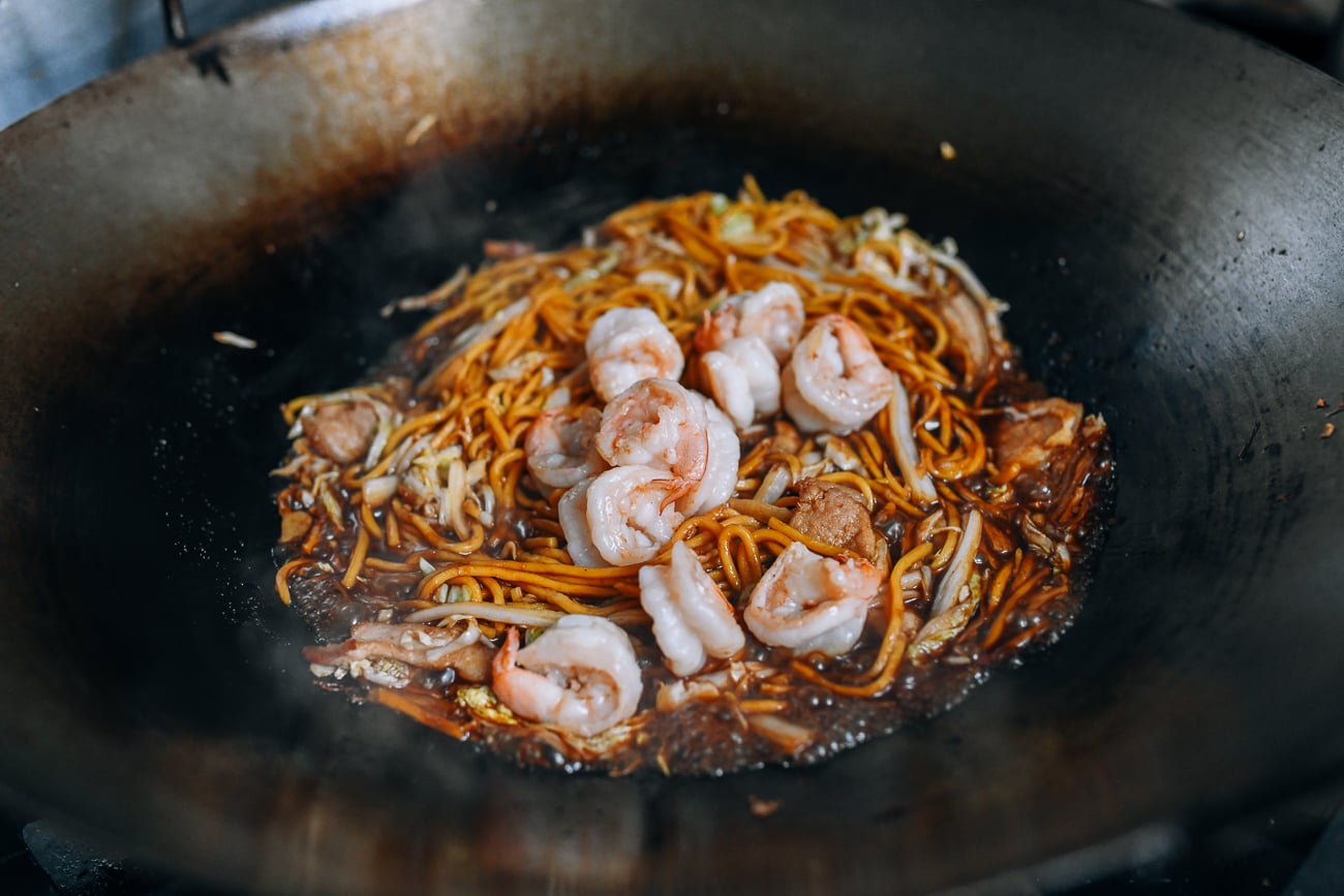 Adding shrimp to noodles in wok