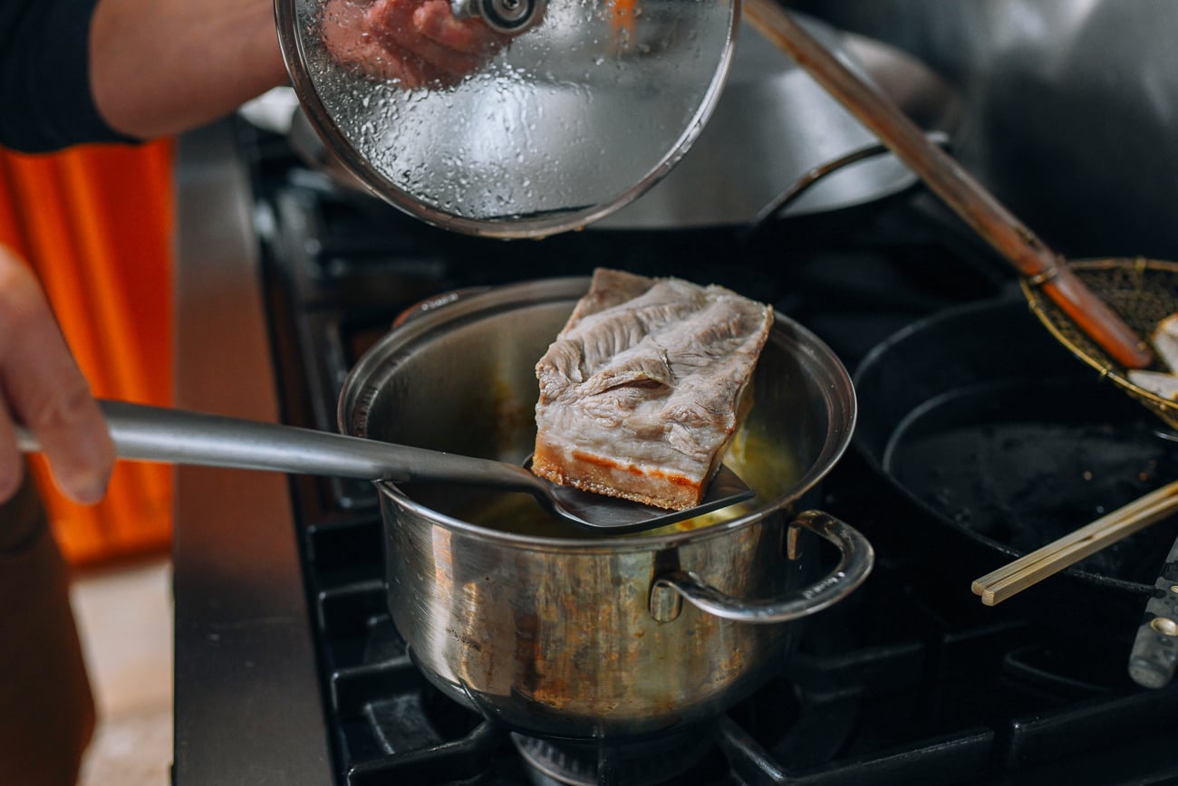 Lowering pork belly into pot of oil