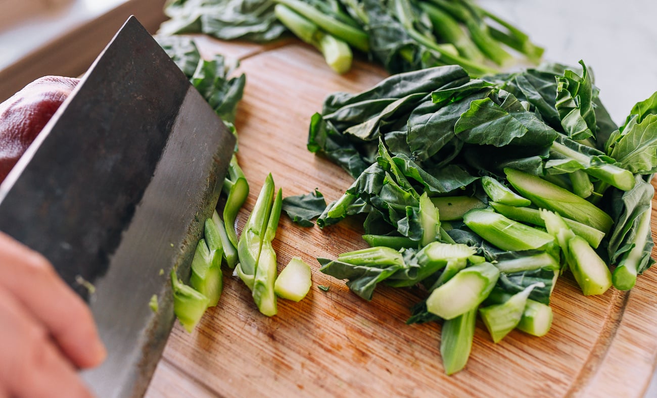 Slicing stalks of gai lan with cleaver