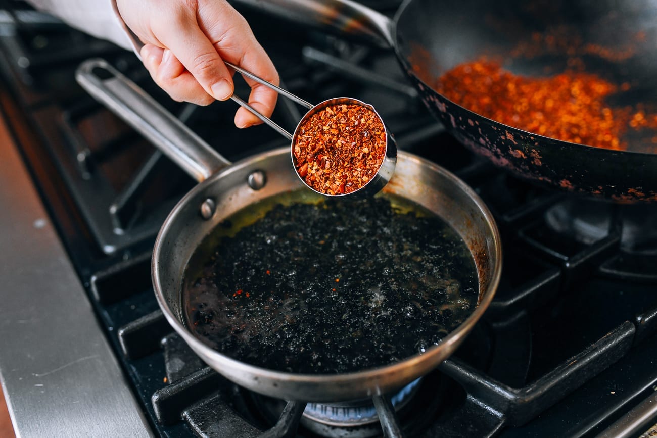 Adding chili flakes to black beans in oil
