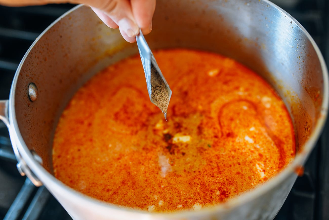 Adding seasoning packet to pot with laksa paste, brown sugar, water, coconut milk
