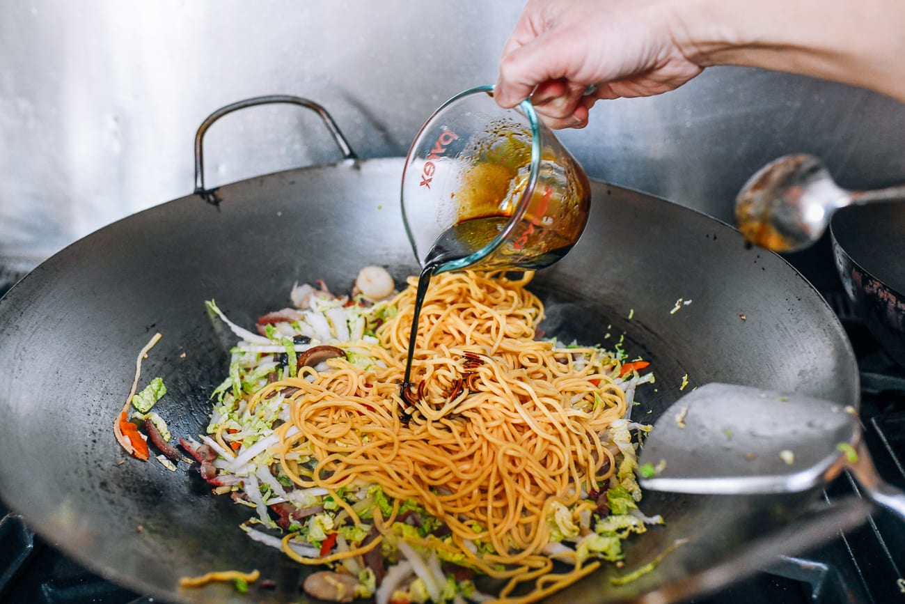 Pouring sauce mixture over lo mein noodles in wok