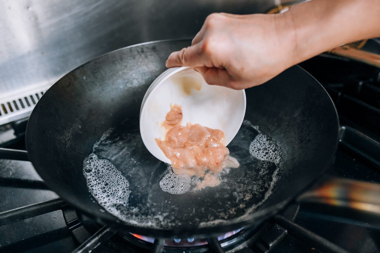 Adding velveted chicken to boiling water in wok