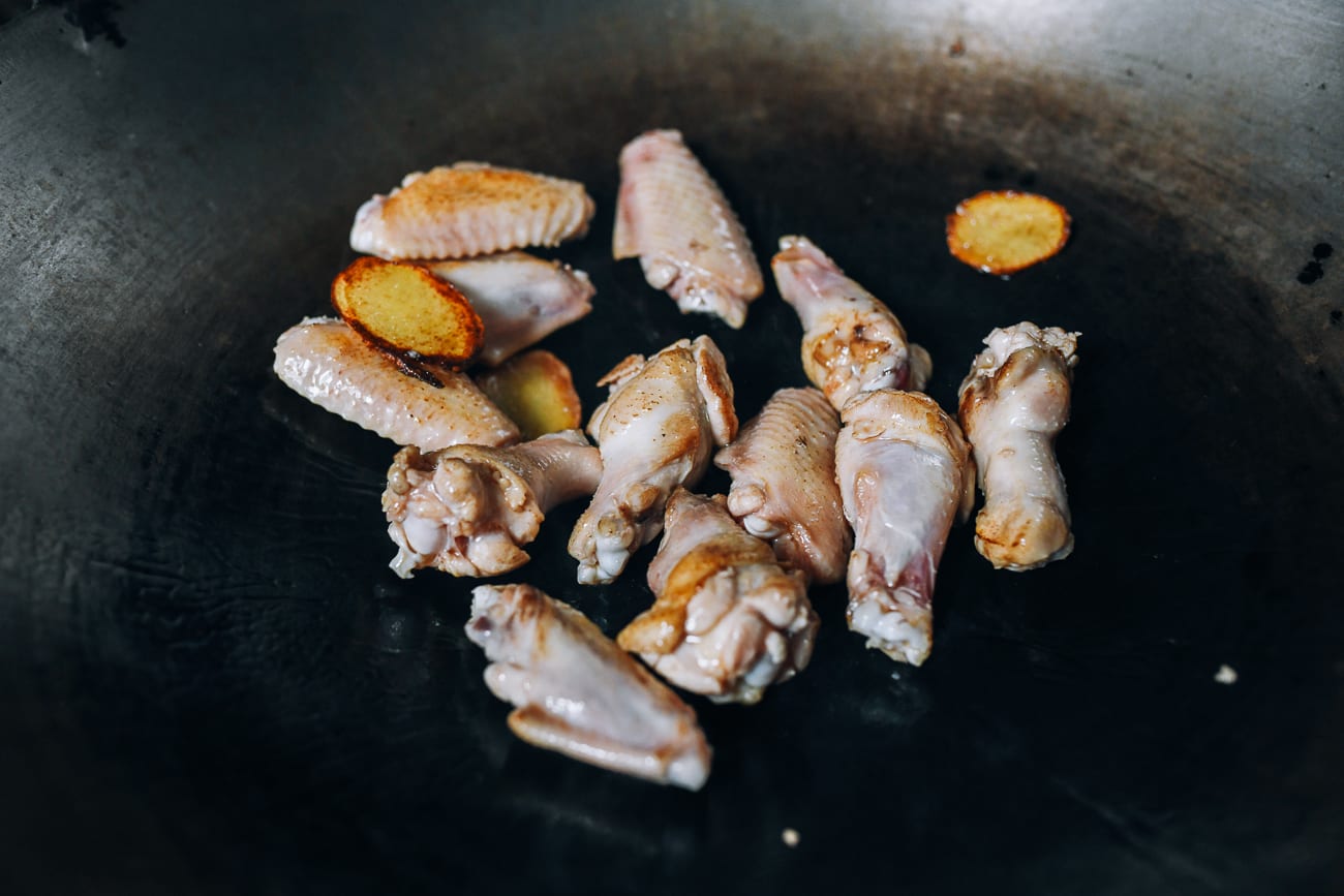 Frying chicken wing pieces with oil and ginger in wok