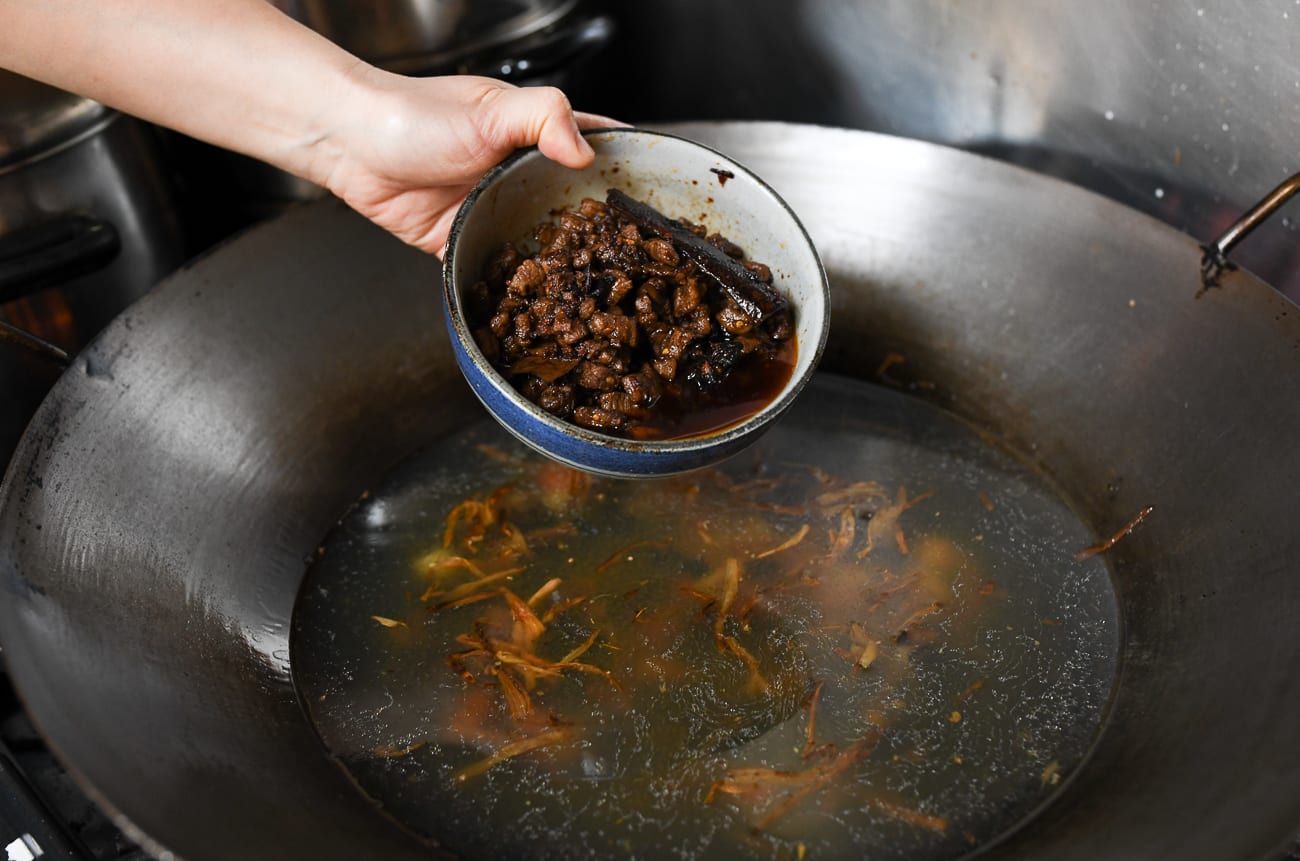 Adding meat sauce to wok with stock