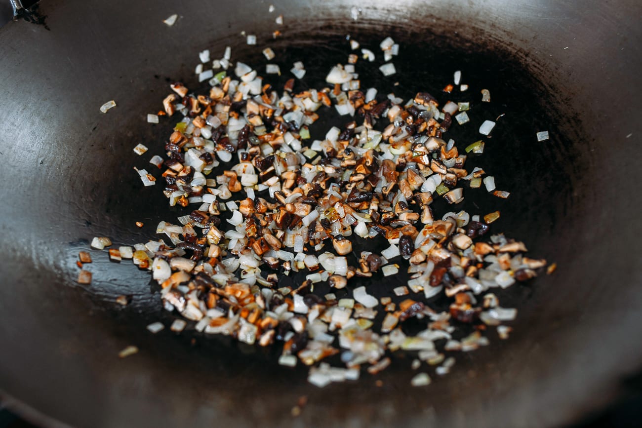 Adding dried shiitake mushrooms to shallots in wok